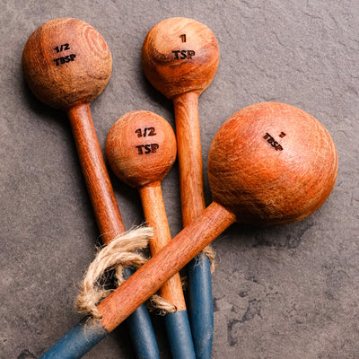 Close up of 4 hand carved wooden measuring spoons with a hand painted blue base, tied together with a jute string