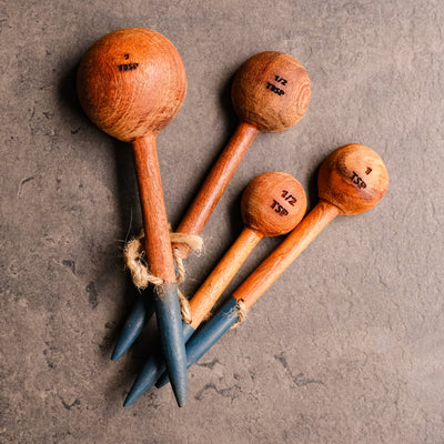 4 hand carved wooden measuring spoons with a hand painted blue base, tied together with a jute string